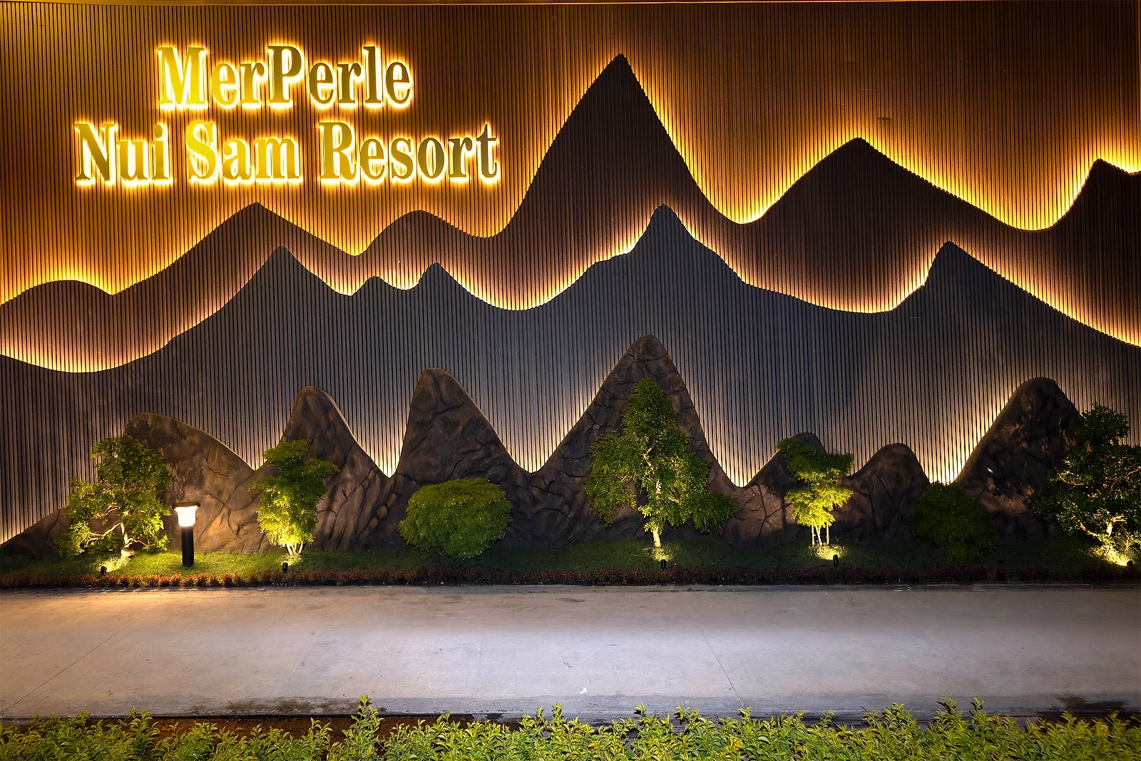 Biển tên MerPerle Nui Sam Resort sáng đèn trên tường phù điêu lúc tối