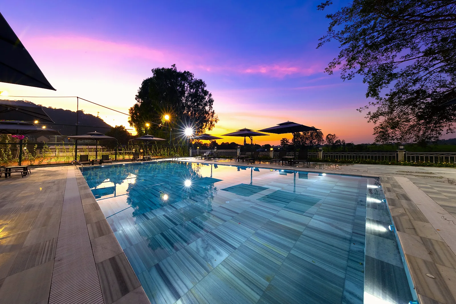 Hồ bơi ngoài trời của MerPerle Nui Sam Resort lúc hoàng hôn, phía sau là dáng Núi Sam