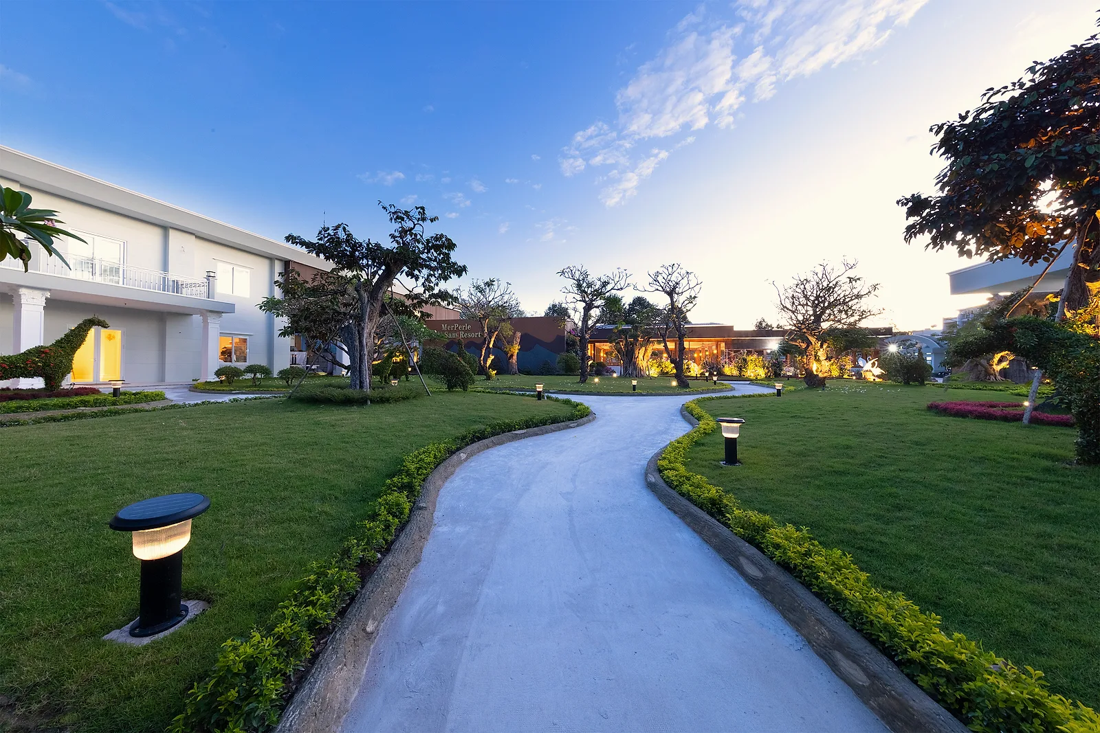 Lối đi trong vườn MerPerle Nui Sam Resort lúc chạng vạng, dẫn tới bức tường mang tên resort